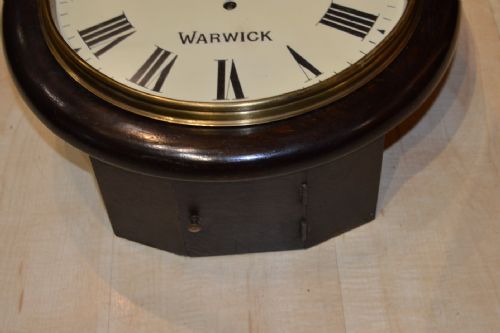 fig 1. A circular Victorian wall clock featuring a dark wood surround, a cream dial with black Roman numerals, a brass bezel, and black hands.
