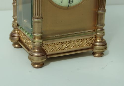 fig 1. A 19th-century brass carriage clock featuring fluted corner columns, intricate fretwork borders, bevelled glass panels, and an overhead carrying handle.