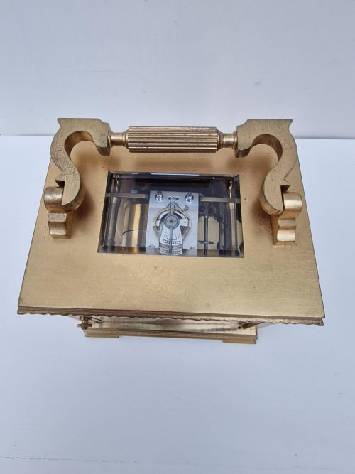 fig 1. A brass carriage clock featuring an oval dial face with black Roman numerals and a decorative scrolled handle.