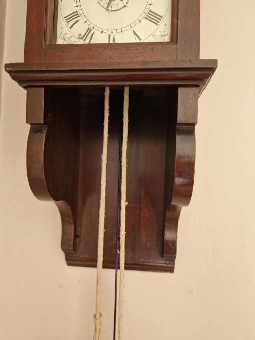 fig 1. A Georgian mahogany hooded wall clock featuring an arched painted dial with Roman numerals, exposed hanging cylindrical lead weight, and brass pendulum bob.