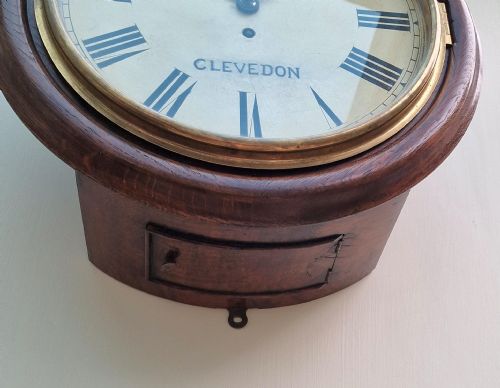 fig 1. A circular antique wall clock featuring a mahogany wooden surround, hinged brass bezel, and off-white painted dial inscribed with J.C. Ralls Clevedon.