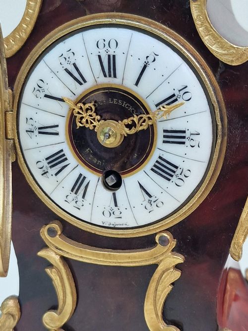 fig 1. A miniature Louis XV style mantel clock featuring a dark red tortoiseshell case adorned with ornate gilt bronze Rococo mounts and a white enamel dial.