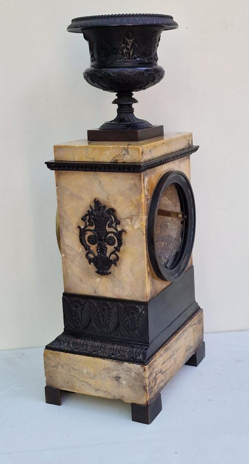 fig 1. A rectangular Sienna marble mantel clock featuring a dark patinated bronze classical urn finial, a gilt dial with Roman numerals, and detailed bronze corner mounts.