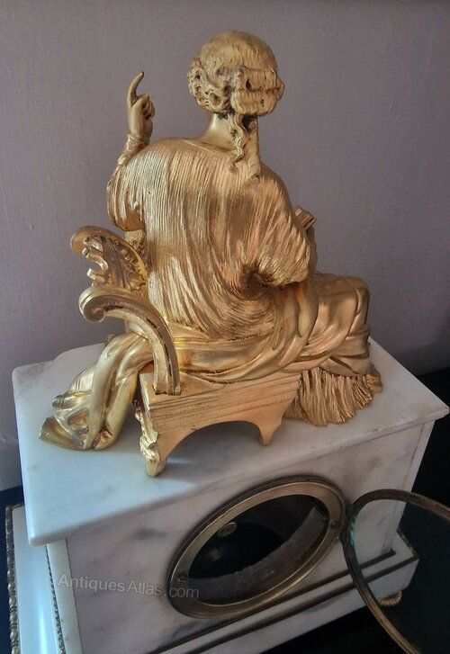 fig 1. A French Neoclassical white marble mantel clock featuring a gilt bronze figure of a seated woman reading a book with a child at her knee.