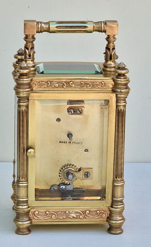 fig 1. An antique brass carriage clock featuring bevelled glass panels, fluted corner columns, ornate foliage borders, and a white dial with Roman numerals.