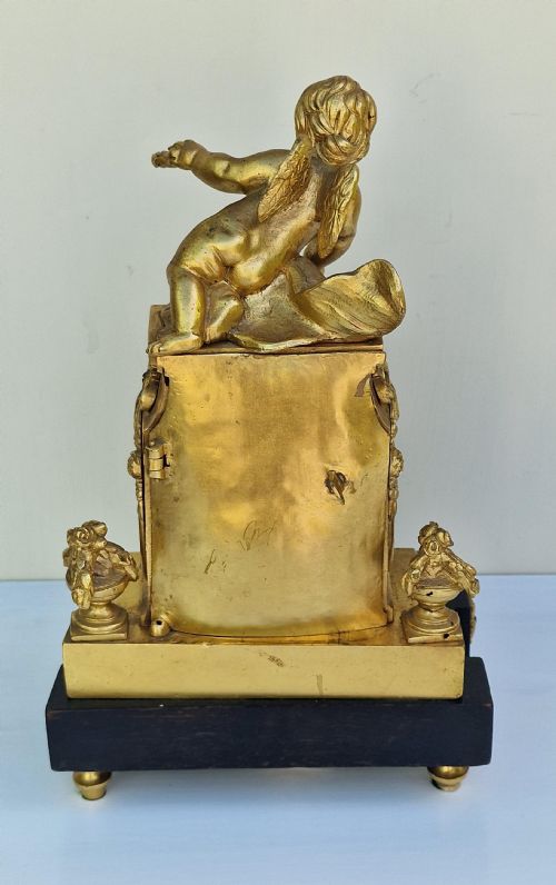fig 1. An antique French gilt bronze mantel clock surmounted by a cherub figure resting above a circular white enamel dial with Roman numerals on an ebonised base.