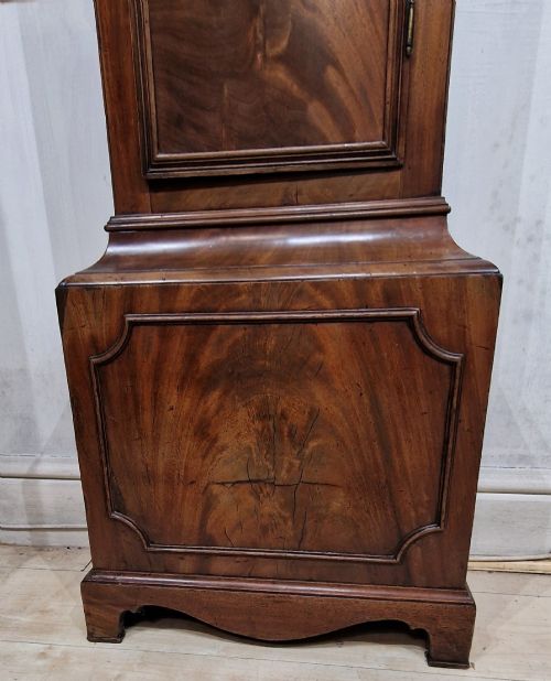 fig 1. A tall Georgian flame mahogany longcase clock featuring an arched hood with brass finials, reeded columns, and a brass and silvered dial.