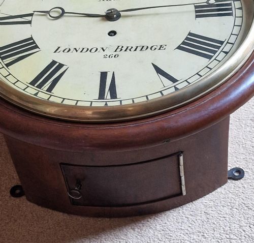 fig 1. A circular antique mahogany wall clock featuring a cream dial with black Roman numerals and a hinged brass bezel.