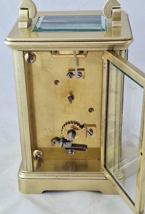 fig 1. A rectangular brass carriage clock featuring a white enamel dial with Roman numerals, blued steel hands, bevelled glass panels, and a hinged carrying handle on top.