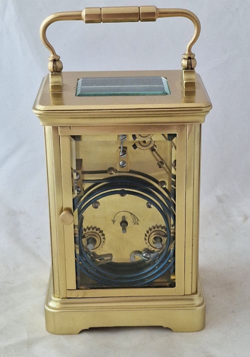 fig 1. A brass carriage clock featuring bevelled glass side panels, a white enamel dial with black Roman numerals, and a top carrying handle.