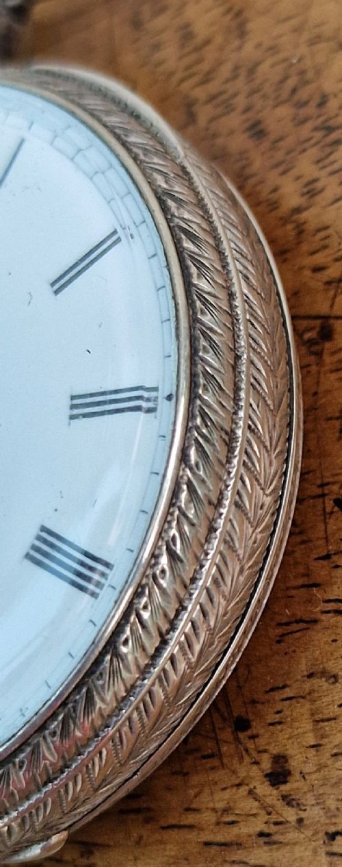 A Victorian silver open-face pocket watch featuring a white enamel dial with Roman numerals alongside an accompanying brass winding key. View IV