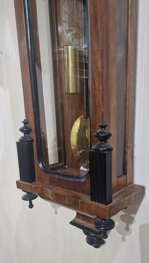 fig 1. An Austrian Vienna regulator wall clock featuring a glazed walnut case with ebonised architectural columns, turned finials, a white Roman numeral dial, and a brass pendulum.