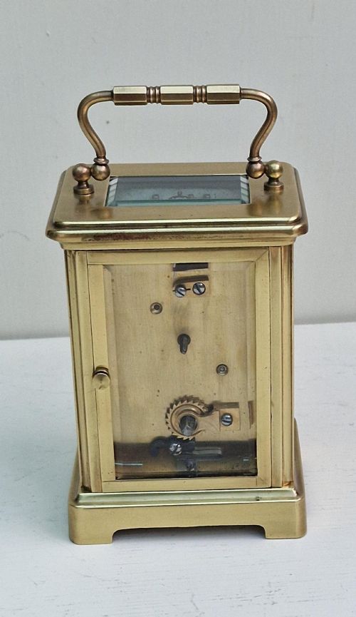 fig 1. An antique French brass carriage clock featuring bevelled glass panels, a white enamel dial with black Roman numerals, and a top carrying handle.