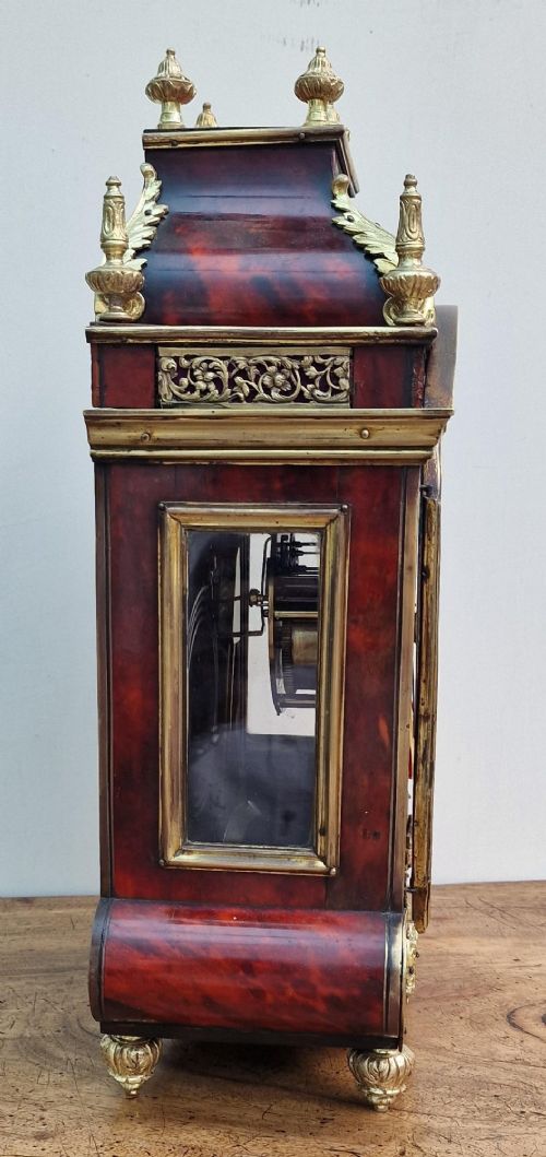 A red tortoiseshell and gilt bronze mantel clock featuring enamel Roman numeral cartouches and cast finials. View VII