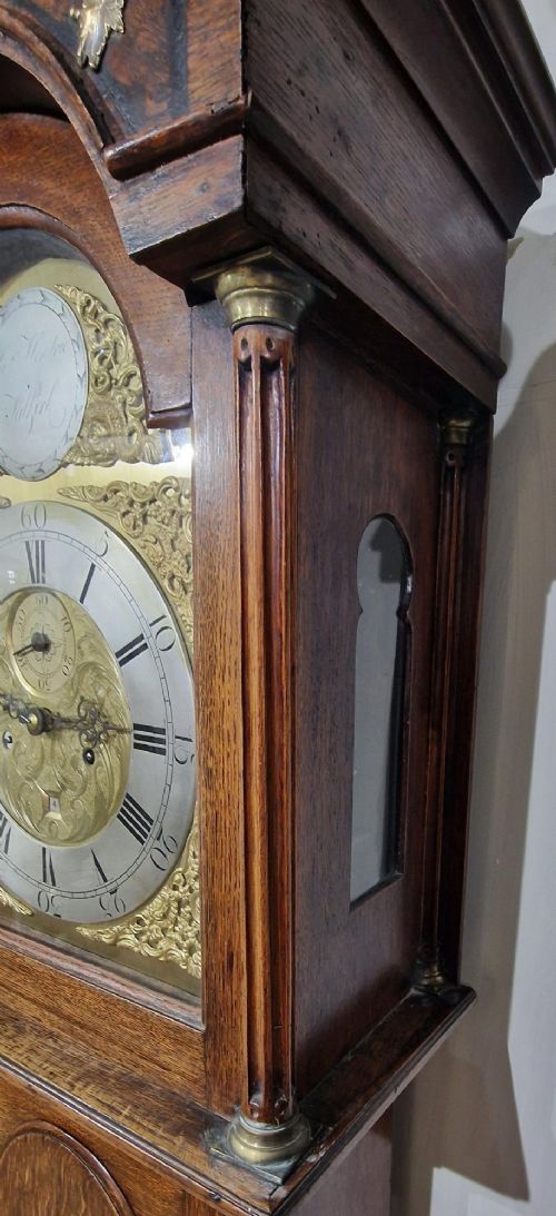 A Georgian oak longcase clock featuring a swan-neck pediment with brass eagle finials and an arched brass dial. View V
