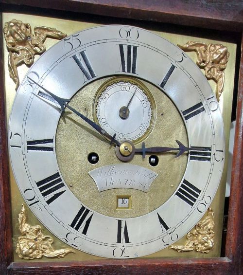 fig 2. A Georgian mahogany grandmother clock featuring a swan-neck pediment, brass rosettes, an engraved brass and silvered dial, and an inlaid wooden trunk case.