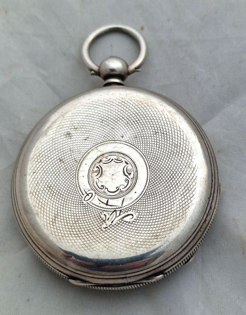 fig 1. An open-face silver pocket watch displaying a white enamel dial with black Roman numerals, a subsidiary seconds dial, and an accompanying brass winding key.