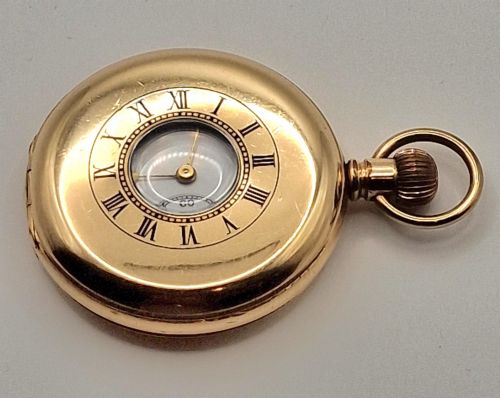 fig 1. An open gold half hunter pocket watch displaying a white enamel dial with black Roman numerals and a small sub-seconds dial at six oclock.