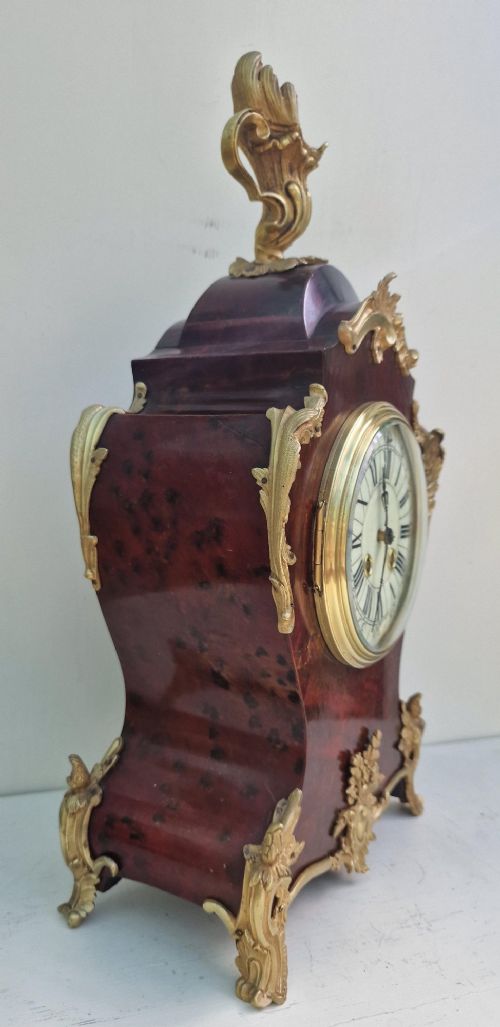 A French Rococo style mantel clock with a dark veneered balloon-shaped case, ornamental gilt-bronze foliage mounts, and a brass-rimmed dial showing Roman numerals. View III