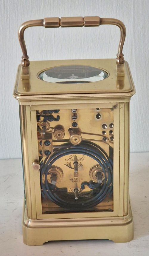 fig 1. A French brass carriage clock with a top carrying handle, white enamel dial with Roman numerals, and clear glass side panels.