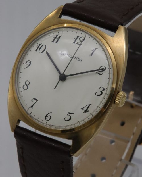fig 1. A 1974 Longines wristwatch with a cushion-shaped 9k yellow gold case, a white dial with black Arabic numerals, and a brown leather strap.
