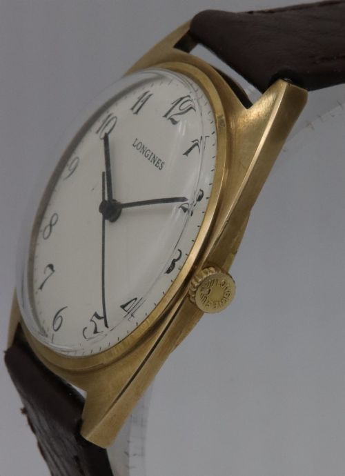 fig 2. A 1974 Longines wristwatch with a cushion-shaped 9k yellow gold case, a white dial with black Arabic numerals, and a brown leather strap.