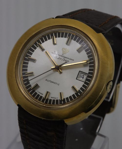 fig 1. A 1970s Jules Jurgensen automatic wristwatch with a gold-toned circular cushion case, white dial, date aperture, and brown textured leather strap.
