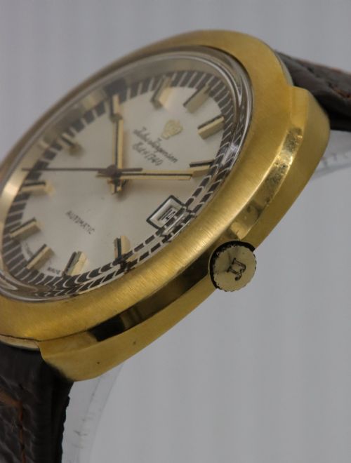 fig 2. A 1970s Jules Jurgensen automatic wristwatch with a gold-toned circular cushion case, white dial, date aperture, and brown textured leather strap.