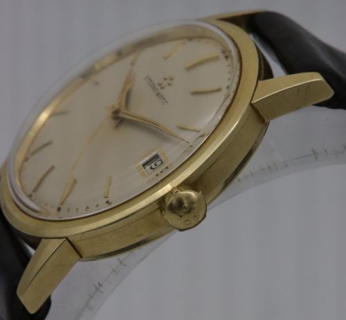 fig 2. A 1957 Eterna-Matic 14K gold wristwatch with an off-white dial, date display window at three oclock, gold baton indices, and a black leather strap.