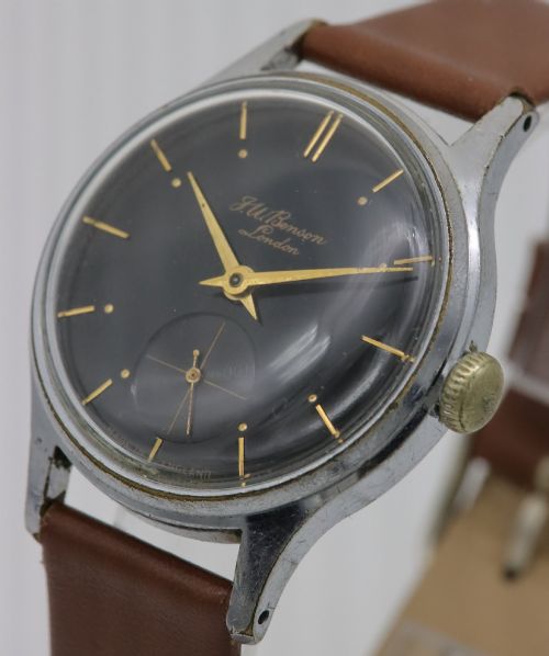 fig 1. A 1950s J.W. Benson wristwatch featuring a black dial, gold-toned hands, a sub-seconds subdial at six oclock, a metallic case, and a smooth brown leather strap.
