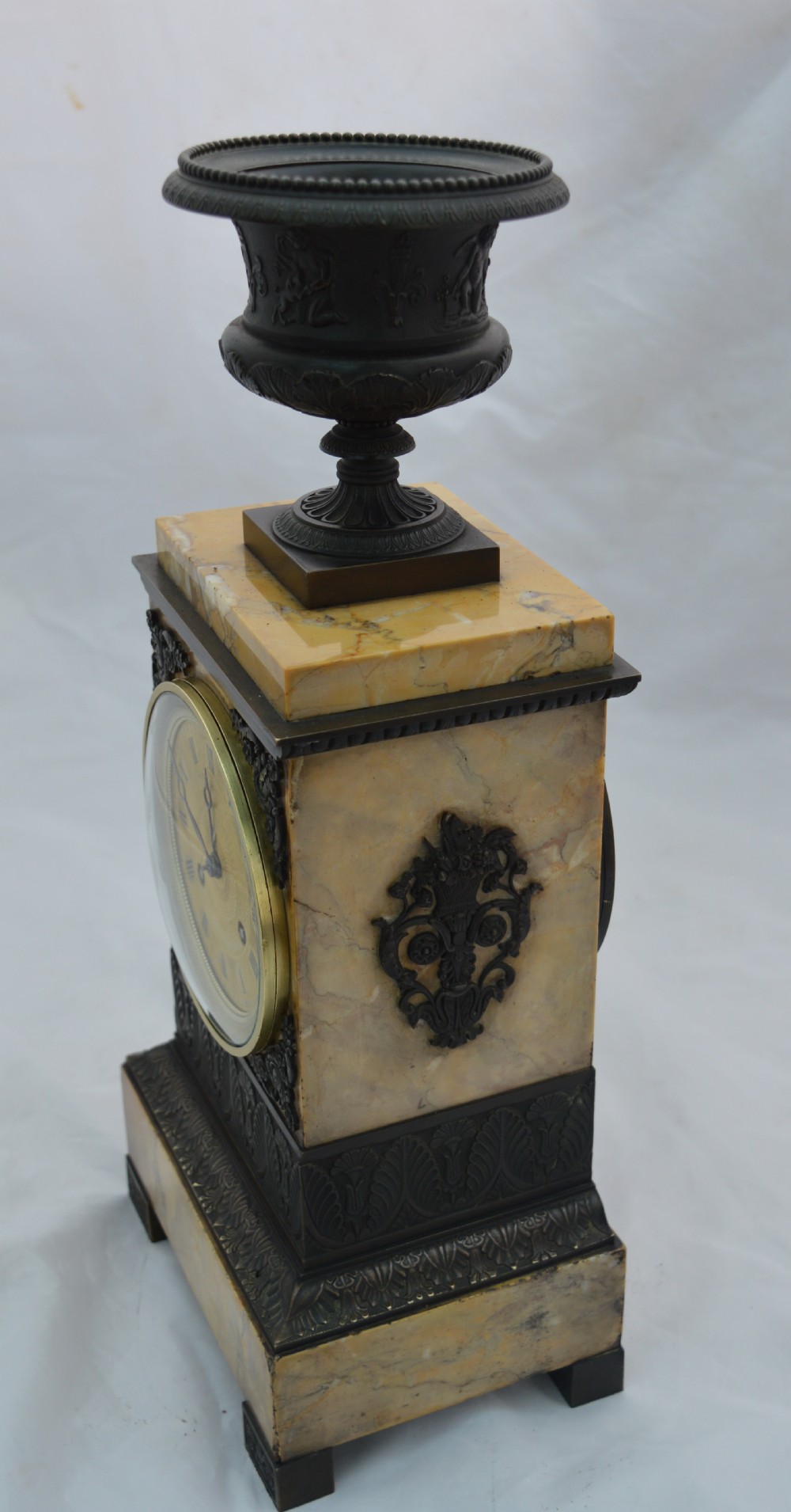 A French Empire mantel clock featuring a yellow marble rectangular body surmounted by a dark patinated bronze classical urn and housing a brass dial with Roman numerals. View II