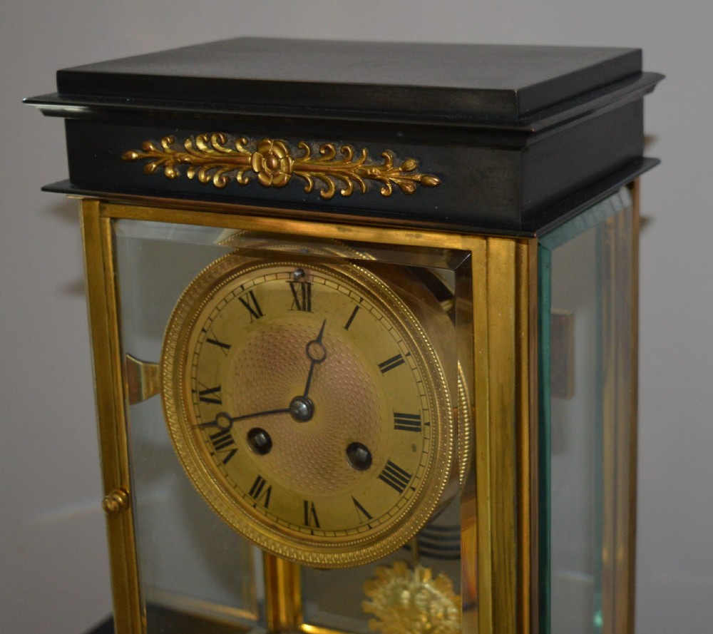 A French four-glass mantel clock framed in brass and black slate flanked by two matching brass candlesticks. View VII