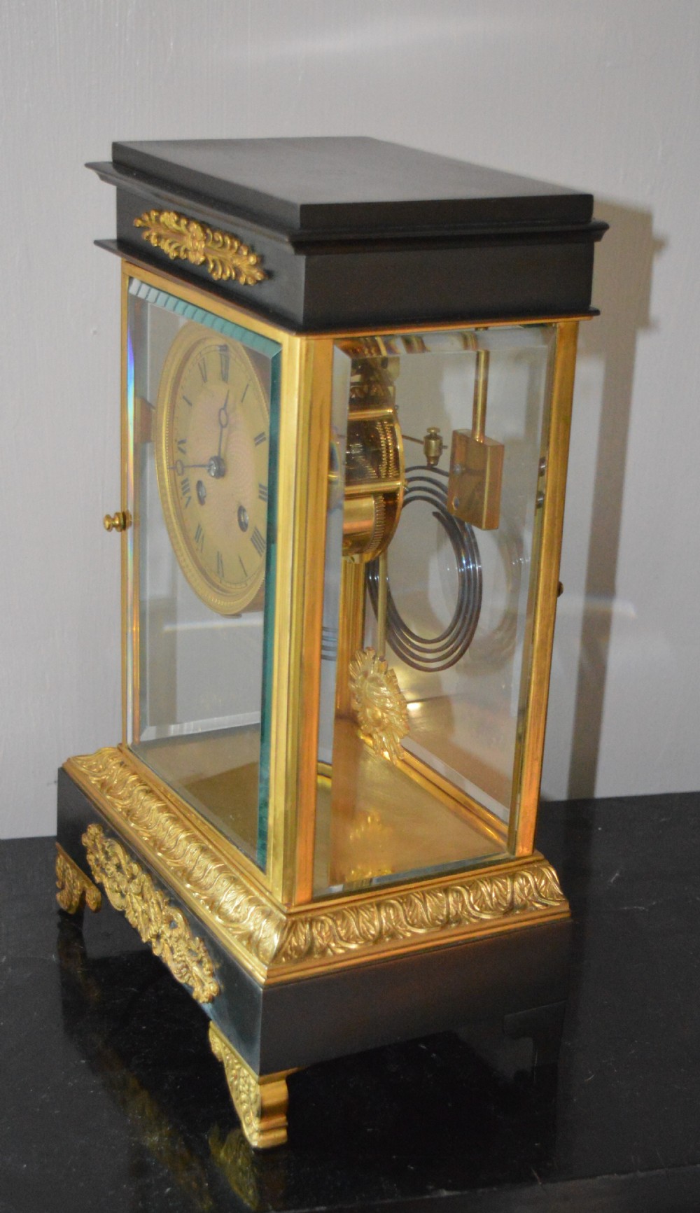 A French four-glass mantel clock framed in brass and black slate flanked by two matching brass candlesticks. View IX