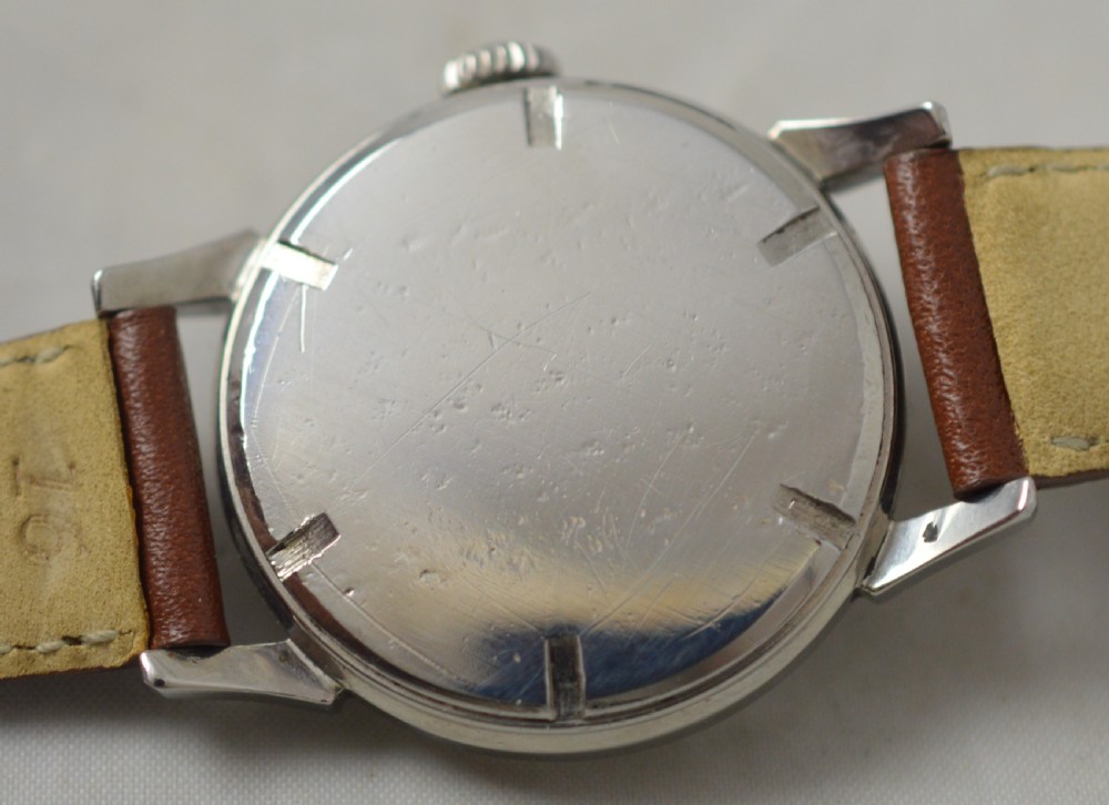 A 1951 Longines stainless steel wristwatch featuring a patinated cream dial with gold-tone Arabic numerals, dart hour markers, and a brown leather strap. View V