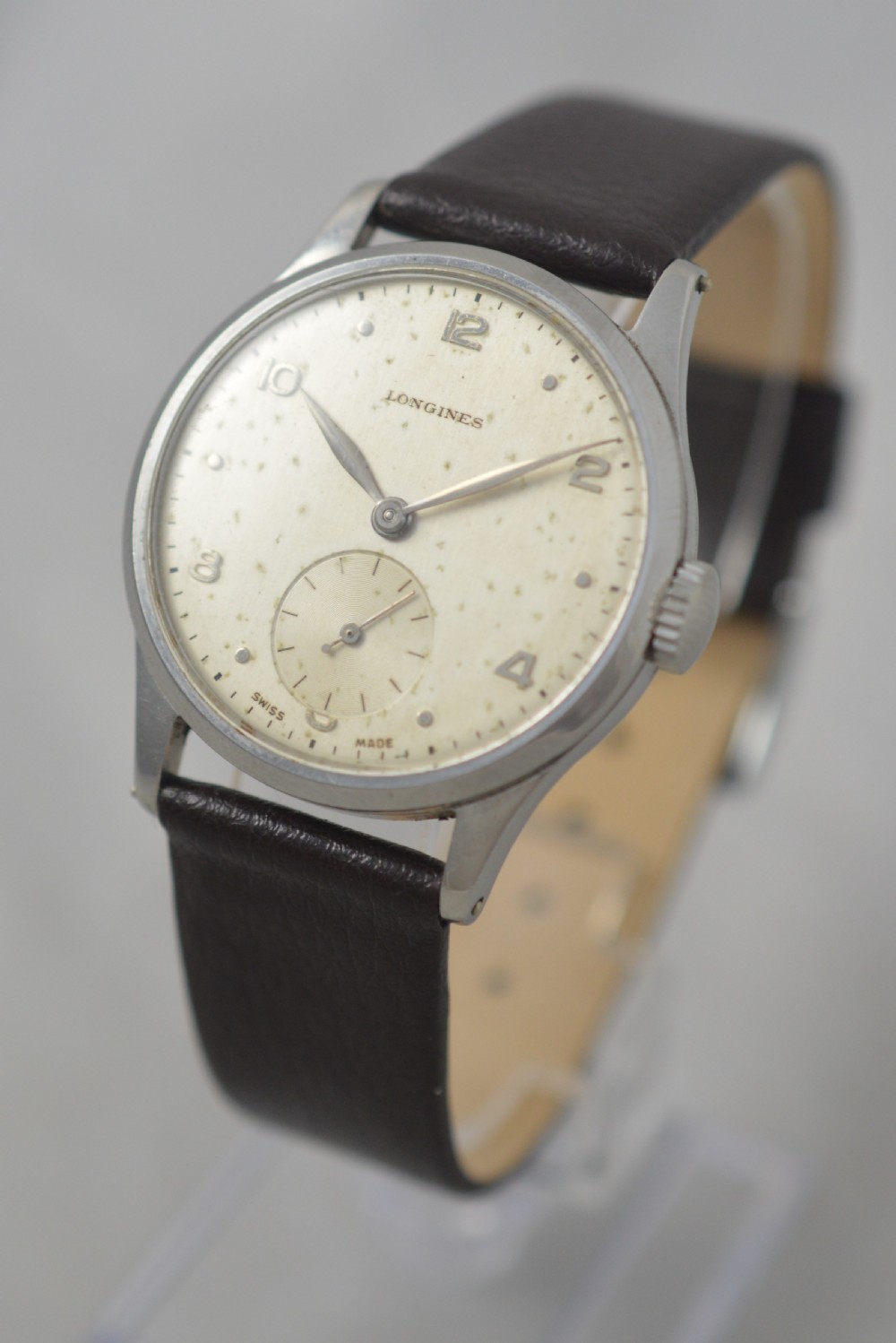 A 1951 Longines gentlemans mechanical wristwatch with a circular stainless steel case, cream dial featuring sub-seconds, and a dark brown leather strap. View IV