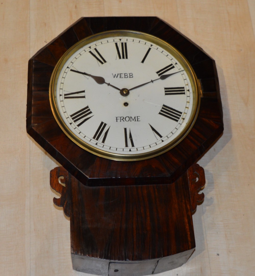 A Victorian drop dial fusee wall clock with an octagonal mahogany frame, cream dial face, black Roman numerals, and carved side ears.