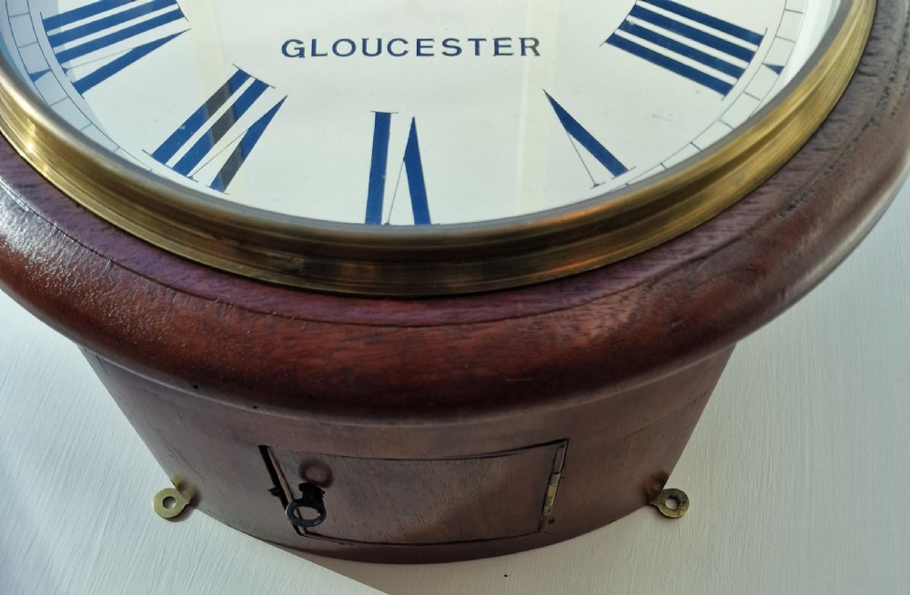 A circular antique mahogany wall dial clock featuring a brass bezel, off-white face with Roman numerals, black hands, and the makers mark H. Gregory Gloucester. View II
