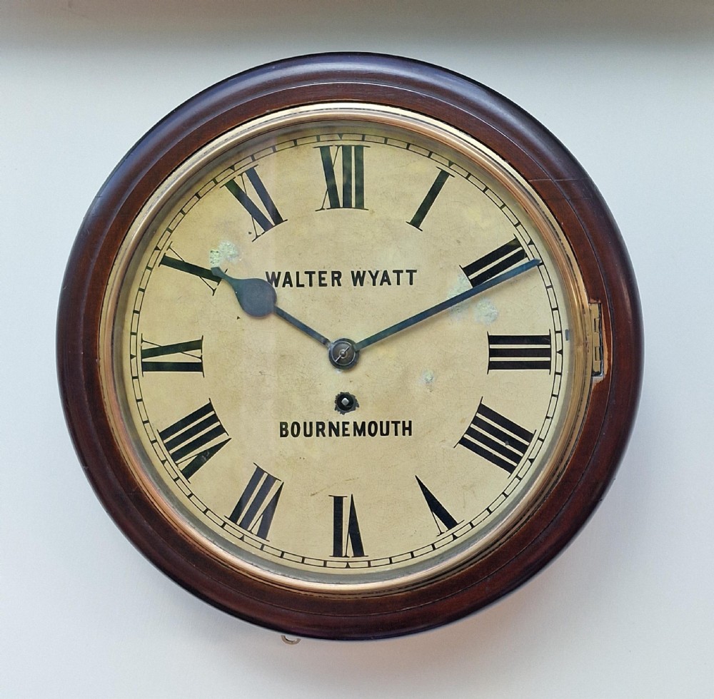 An antique round mahogany fusee wall clock featuring a cream painted dial with black Roman numerals, brass bezel, and maker inscription reading Walter Wyatt Bournemouth.