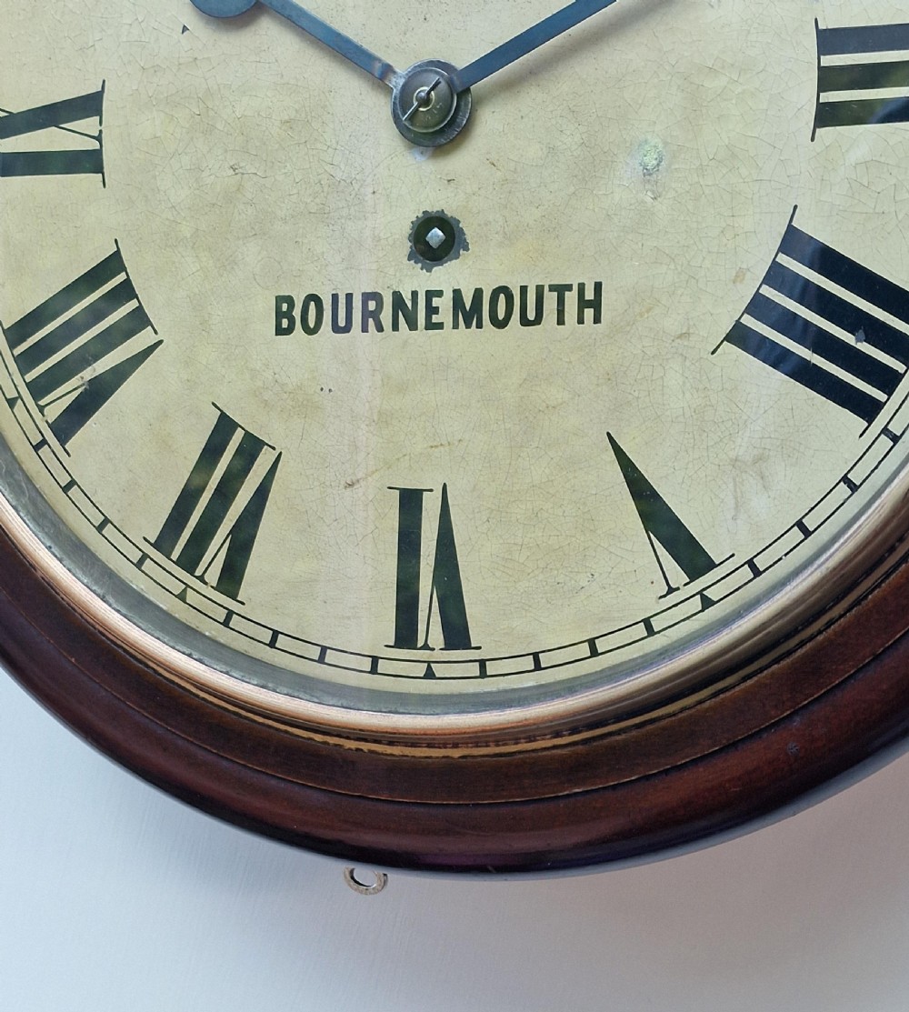 An antique round mahogany fusee wall clock featuring a cream painted dial with black Roman numerals, brass bezel, and maker inscription reading Walter Wyatt Bournemouth. View II