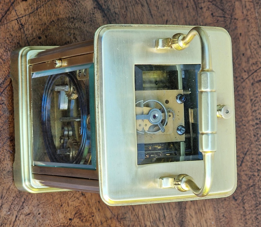A rectangular brass carriage clock featuring bevelled glass side panels, a top carrying handle, a top repeat button, and a white enamel dial with black Roman numerals. View III