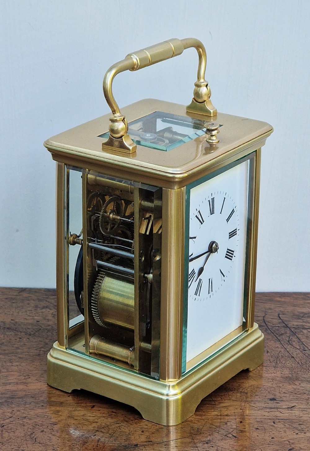 A rectangular brass carriage clock featuring bevelled glass side panels, a top carrying handle, a top repeat button, and a white enamel dial with black Roman numerals. View IV