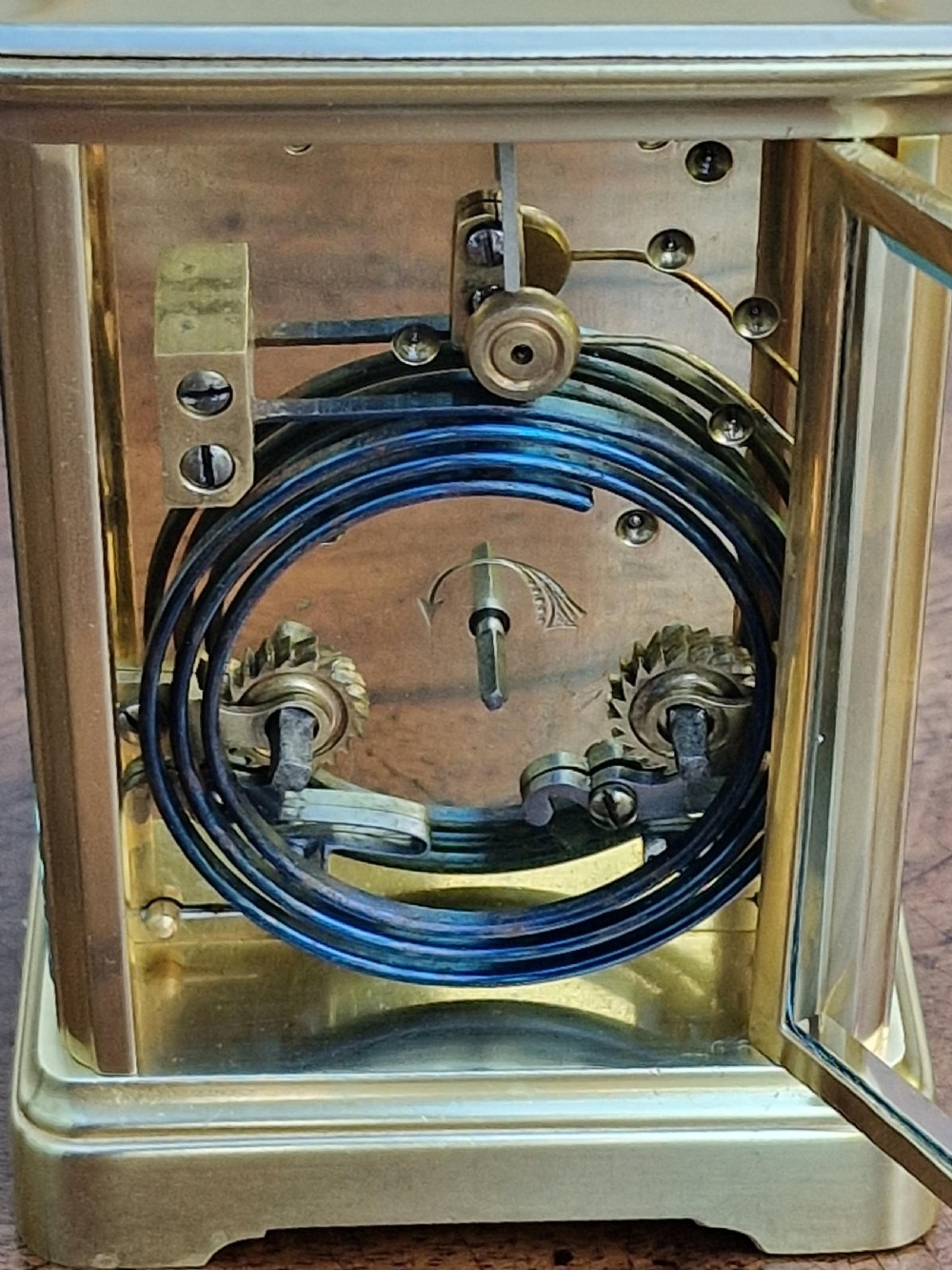 A rectangular brass carriage clock featuring bevelled glass side panels, a top carrying handle, a top repeat button, and a white enamel dial with black Roman numerals. View V