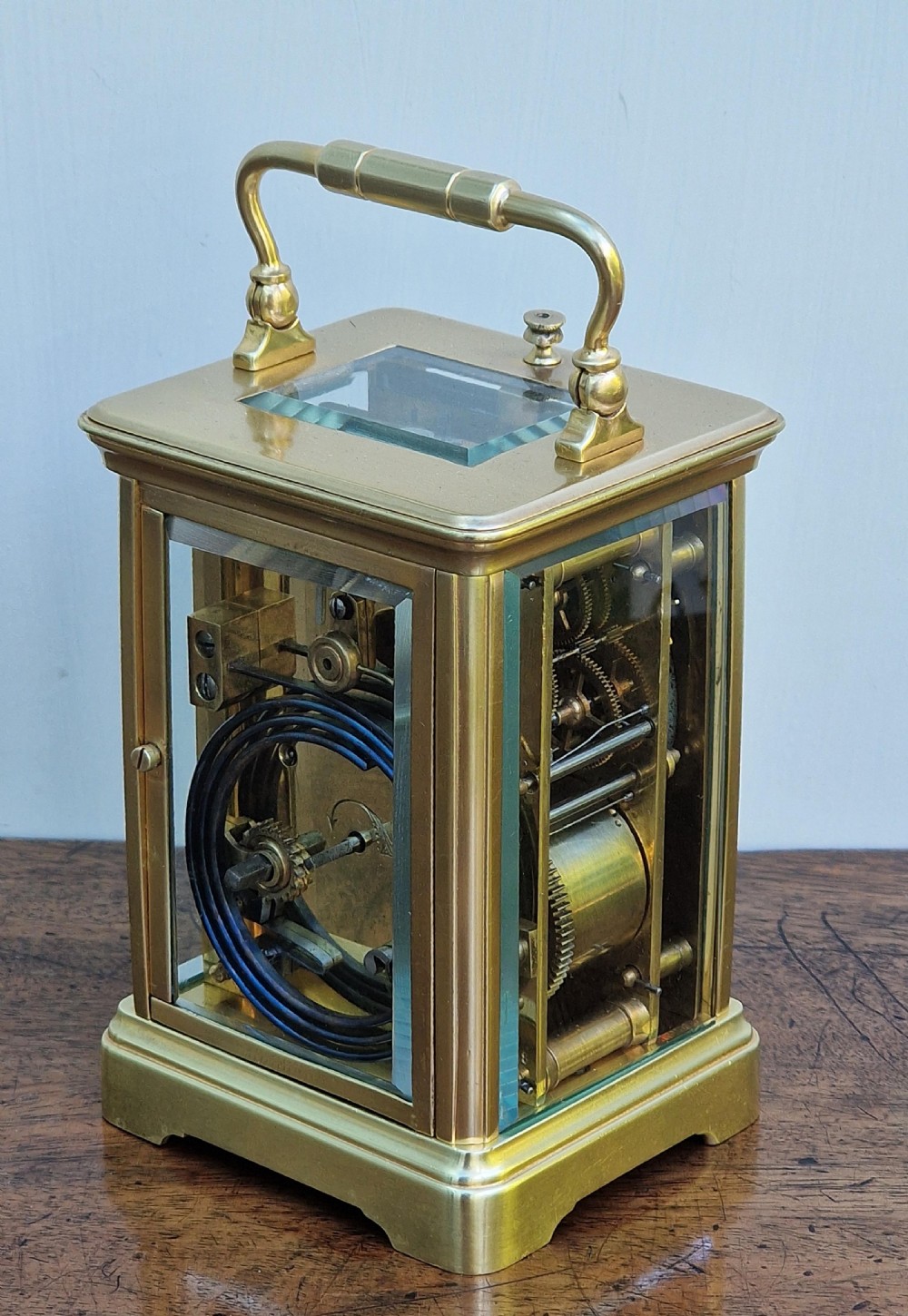 A rectangular brass carriage clock featuring bevelled glass side panels, a top carrying handle, a top repeat button, and a white enamel dial with black Roman numerals. View VI