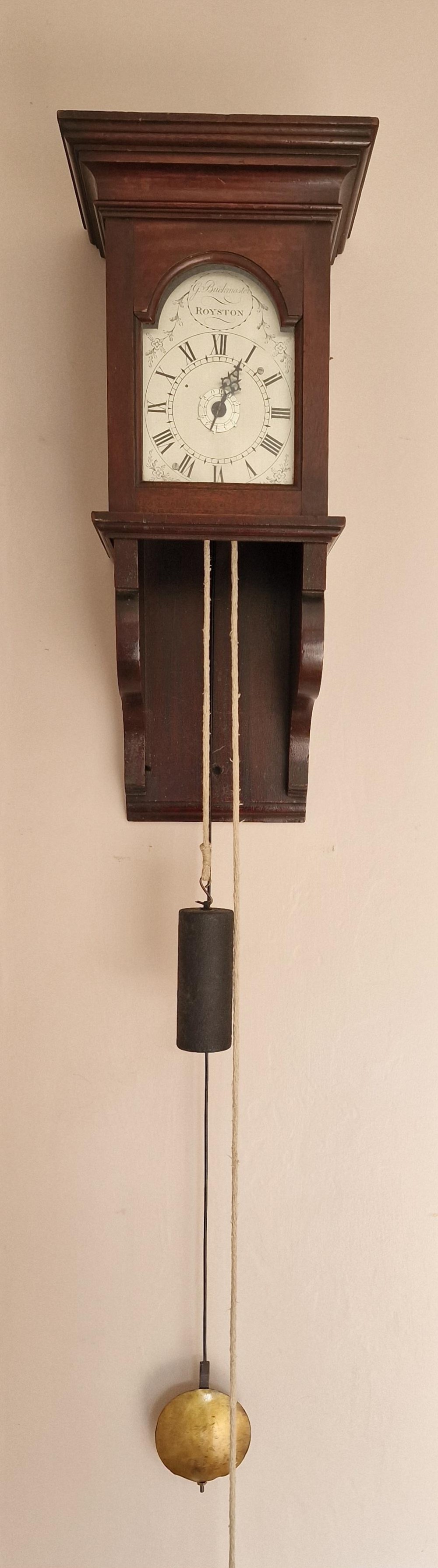 A Georgian mahogany hooded wall clock featuring an arched painted dial with Roman numerals, exposed hanging cylindrical lead weight, and brass pendulum bob.
