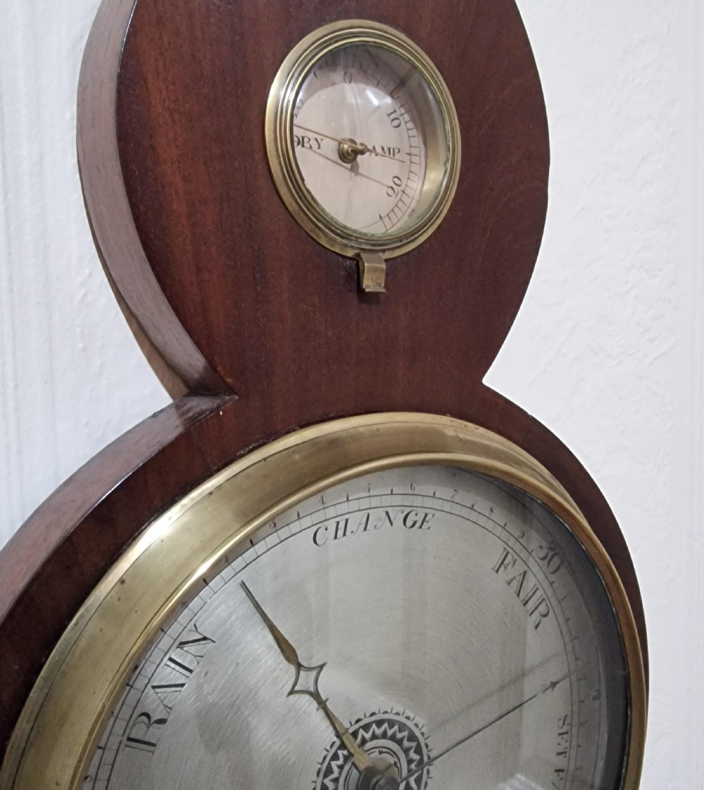 A Georgian mahogany banjo barometer featuring floral patera marquetry, an integrated thermometer tube, and a silvered weather dial in a brass bezel. View IV