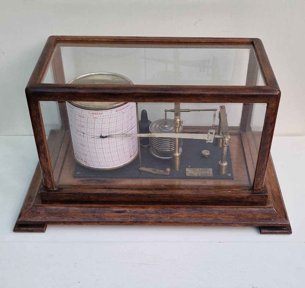 An antique Negretti and Zambra barograph featuring a brass recording mechanism and paper chart drum inside a glazed oak display case.