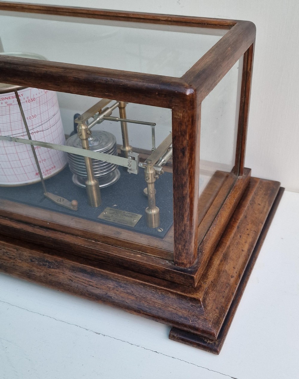 An antique Negretti and Zambra barograph featuring a brass recording mechanism and paper chart drum inside a glazed oak display case. View IV