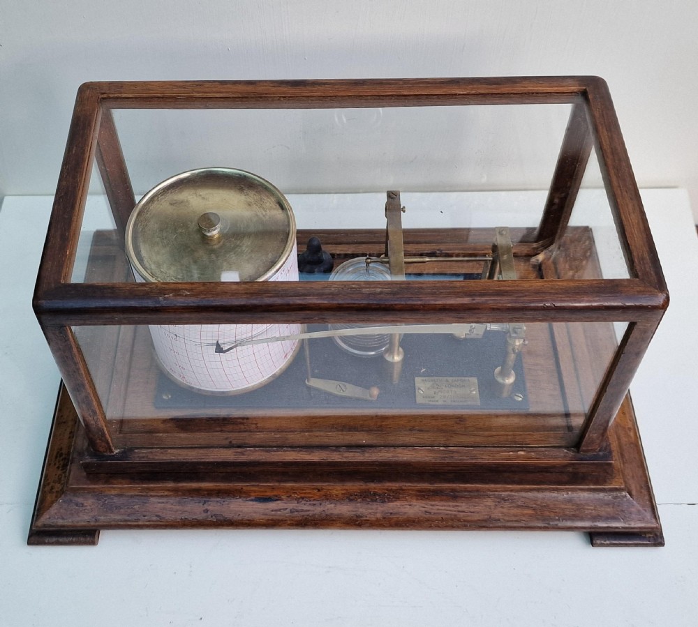 An antique Negretti and Zambra barograph featuring a brass recording mechanism and paper chart drum inside a glazed oak display case. View V
