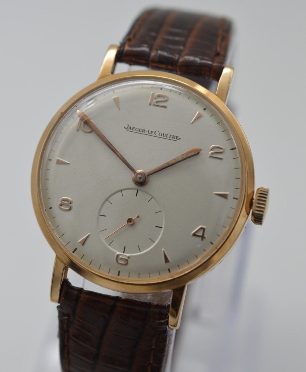 A 1950s Jaeger-LeCoultre wristwatch featuring an 18K rose gold round case, cream dial with rose gold markers, sub-seconds dial at six oclock, and brown leather strap. View III