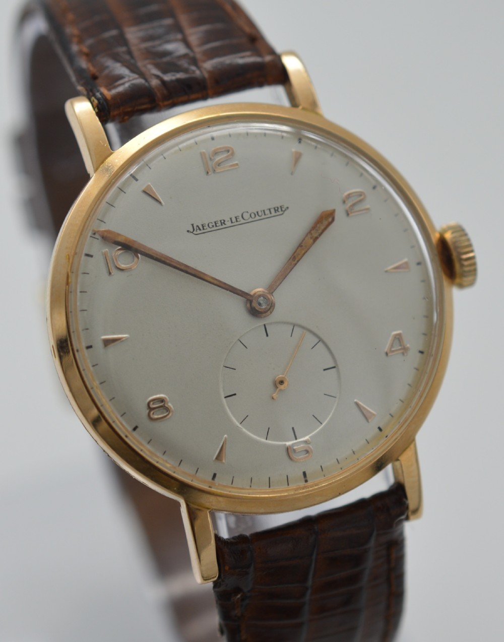 A 1950s Jaeger-LeCoultre wristwatch featuring an 18K rose gold round case, cream dial with rose gold markers, sub-seconds dial at six oclock, and brown leather strap. View IV